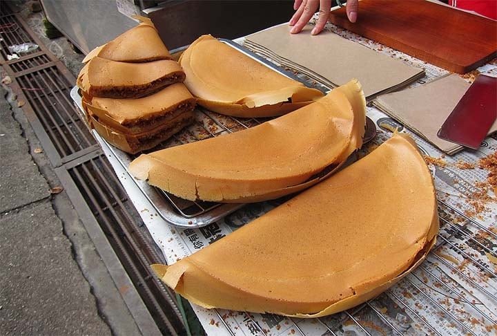 Apam Balik: na Malásia esta receita é feita a partir da mistura de farinha, ovos, açúcar, bicarbonato de sódio, leite de coco e água. Assemelha-se a uma panqueca grossa cozida recheada com amendoim,  açúcar e milho doce.  Reprodução: Flipar
