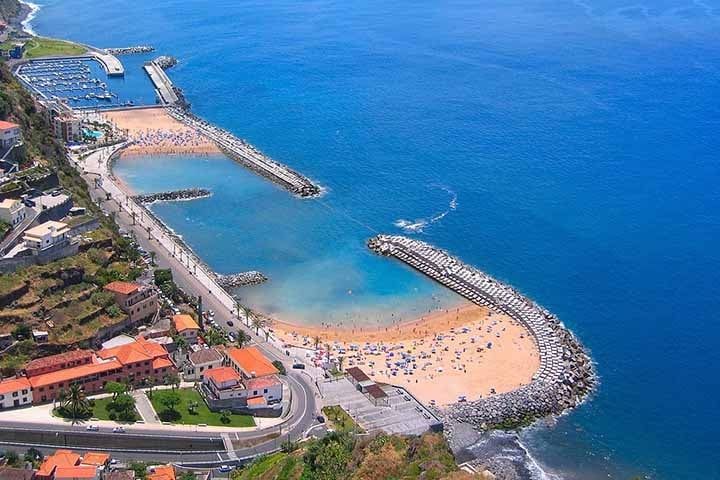 A Praia da Calheta é uma das poucas praias de areia amarela na Madeira. Ela oferece um ambiente mais acessível para os turistas, com águas calmas e várias opções de lazer, como restaurantes e bares. Reprodução: Flipar