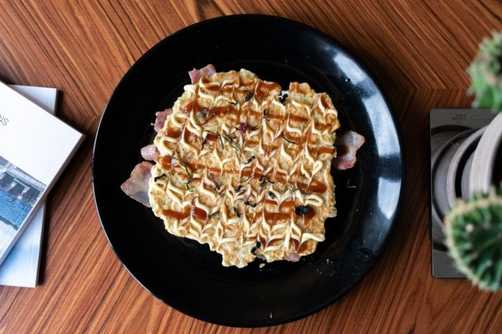 Okonomiyaki: Uma espécie de panqueca japonesa feita com uma massa de farinha e água, combinada com repolho e outros ingredientes, como carne, frutos do mar ou queijo. É cozida em uma chapa e geralmente servida com molho okonomiyaki, maionese e flocos de bonito seco. Reprodução: Flipar